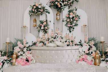 Asılan Lanternli Süslü Beyaz Arkaplan. Beyaz geometrik kemerler, pembe güller ve beyaz bir bankta altın Fas tarzı fenerlerin yer aldığı sofistike bir düğün düzeni..