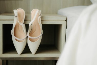Gelinlik Sırtı Ayakkabıları Ahşap Gece Duruşu. Düğün hazırlıkları sırasında modern ahşap bir sehpanın üzerinde kristal süslerle sergilenen bir çift beyaz gerdanlık gerdanlık ayakkabısı. 30 Aralık 2023, Kuching, Sarawak, Malezya.