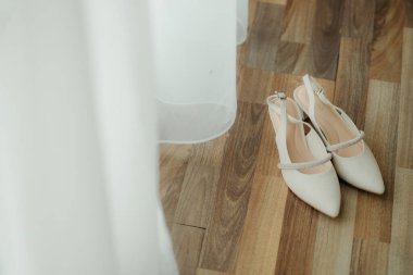 Crystal Straplı Beyaz Gelinlik Ayakkabıları. Beyaz perdenin yakınındaki ahşap bir zemine pırıltılı yapay elmaslı bir kayışla fildişi renkli bir çift işaret parmağı gelinlik ayakkabısı. 30 Aralık 2023, Kuching, Sarawak, Malezya.