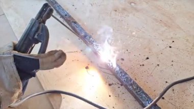 Bir işçinin uzun metal bir levhayı kaynak yaparak parlak kıvılcımlar ve yoğun bir kaynak yayı oluşturduğu yakın çekim görüntüleri..