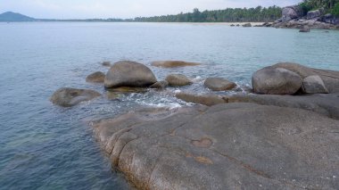 View of the calm ocean horizon from the rocky shore of Siangau Beach. The water gently washes over the granite stones in the foreground.
