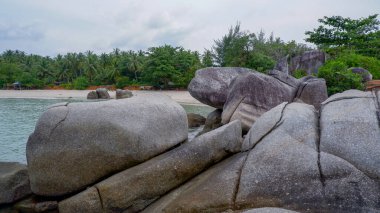 Siangau Sahili 'nin beyaz kumlarında yemyeşil hindistan cevizi ağaçları ve bulutlu gökyüzü bulunan eşsiz granit kaya oluşumları..