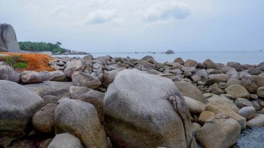 Wide angle view of massive granite boulders mixed with red earth along the coastline of Siangau Beach, facing the open sea, Indonesia