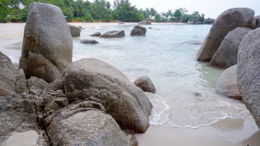 Dağılmış granit kayaları çevreleyen berrak tropikal deniz suyu kumlu bir sahil boyunca sakin ve doğal bir ada deniz manzarası yaratır..
