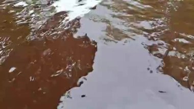 Kahverengi tatlı su nehir yüzeyinin doğal çökelti rengi ve akış şekilleriyle üst görüntüsü. Doğal su dokusu çevresel, jeolojik ve doğa arka plan kavramları için kullanışlıdır