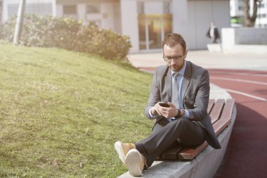 Bankta dinlenirken akıllı telefonunu kullanan işadamı   