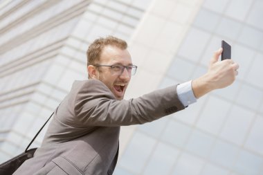 Young professional taking selfie in front of the blue glass business building  