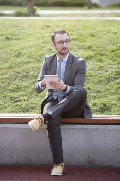Joven hombre de negocios usando un dispositivo de tableta en un banco en el parque — Foto de Stock