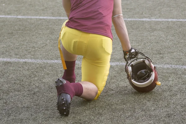 Футболист стоит на коленях и держит спортивный шлем на игровом поле — стоковое фото