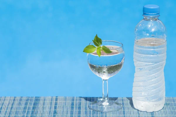 Glass and bottle of water on bamboo straw mat — Stock Photo, Image