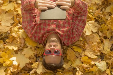 Sarı yaprakları ile kaplı ve dijital tablet cihaz kullanarak yerde yatan adam