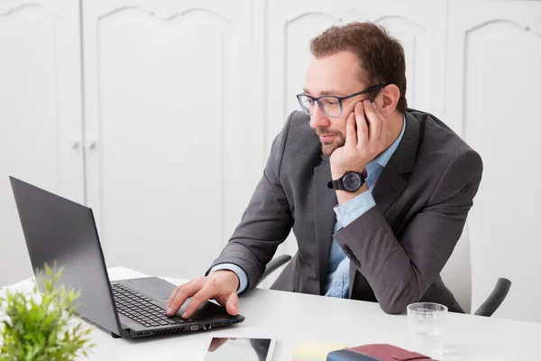 Empresario sentado en el escritorio y mirando la pantalla del ordenador portátil — Foto de Stock