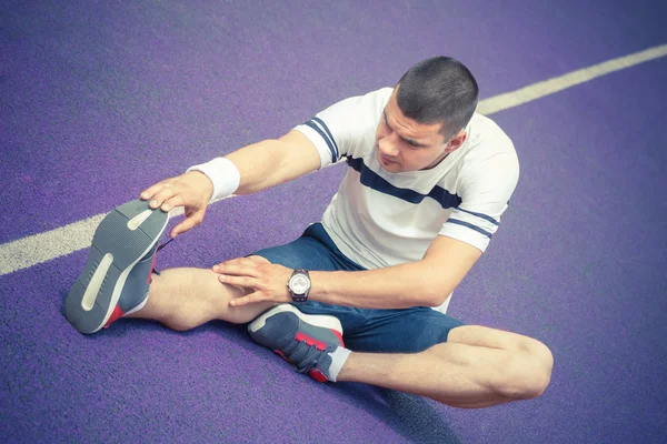 Homem esticando a perna na pista de corrida — Fotografia de Stock