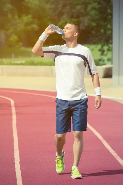 Jogger andando na pista de corrida e água potável da garrafa — Fotografia de Stock