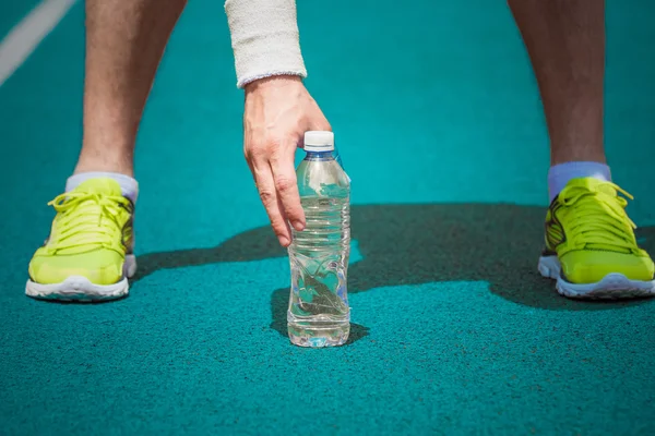 Close up de corredor masculino segurando garrafa de plástico de água na pista de corrida — Fotografia de Stock