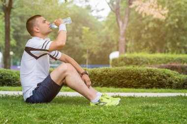 Çim ve içme suyu üzerinde oturan koşucu