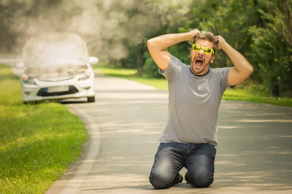 Desperate guy kneeing on the road because his car is broken — Stock Photo, Image