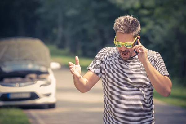 Mann telefoniert im Hintergrund mit Smartphone und kaputtem Auto — Stockfoto