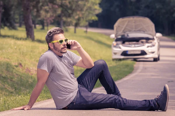 Mann telefoniert im Hintergrund mit Smartphone und kaputtem Auto — Stockfoto