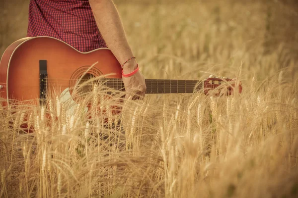 Man håller gitarr och gå igenom vete fält — Stockfoto