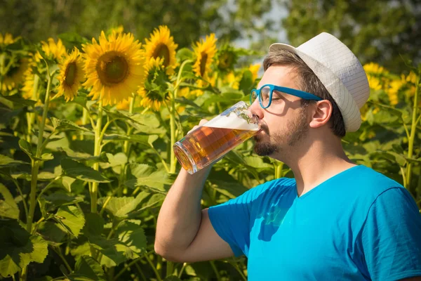 Jonge hipster bier drinken in zonnebloem veld — Stockfoto