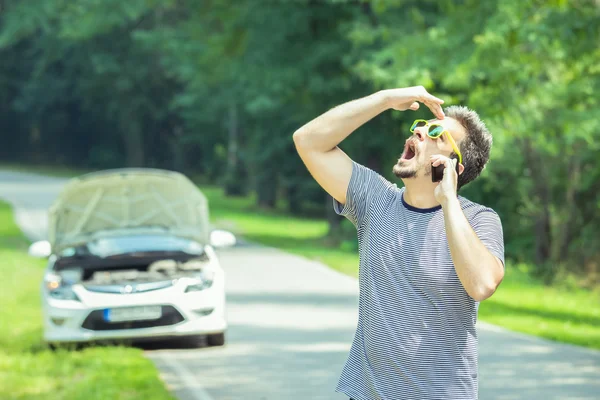 Mann telefoniert im Hintergrund mit Smartphone und kaputtem Auto — Stockfoto