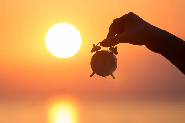 Mão feminina segurando despertador ao nascer do sol — Fotografia de Stock