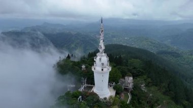 Hızlı hareket eden sis ve bulutlarla çevrili beyaz sarmal kulenin hava görüntüsü kısmen verimli dağlık araziyi ortaya çıkarıyor.