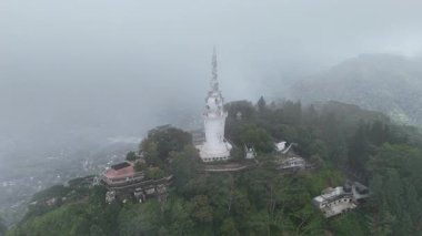 İnsansız hava aracı, Sri Lanka 'nın merkezindeki yeşil dağları ve ormanları kaplayan sis bulutuyla beyaz spiral kulenin üzerinde uçuyor.