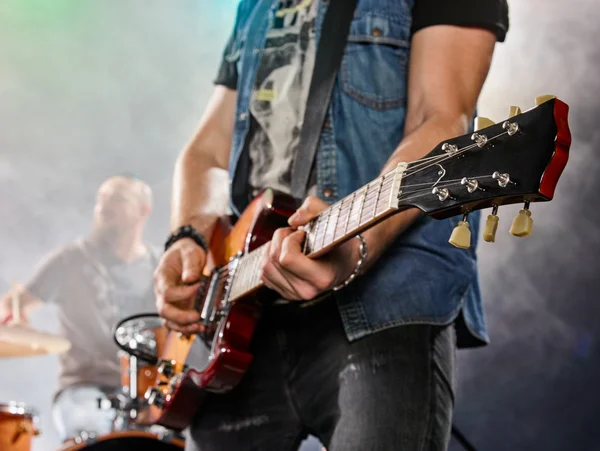 Rock band performs on stage. Guitarist and drums.