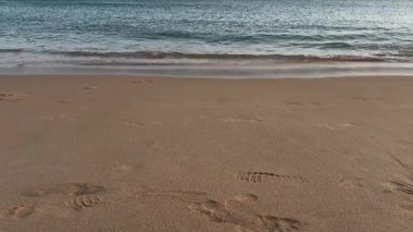 Close-up view of a person strolling along wet sandy beach after rainfall. Reflections shimmer on the surface as gentle waves roll in, creating a calm and peaceful seaside atmosphere