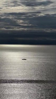Huzurlu yalnız tekne dramatik bulutlu gökyüzünün altında parıldayan denizde sürükleniyor..