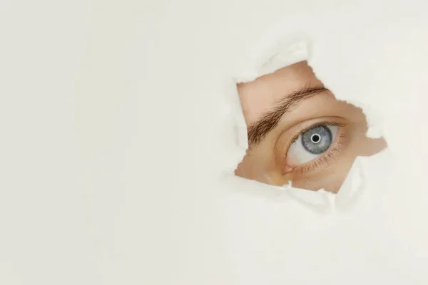 Blue eyed girl looking through ripped paper Template for eye care products design.
