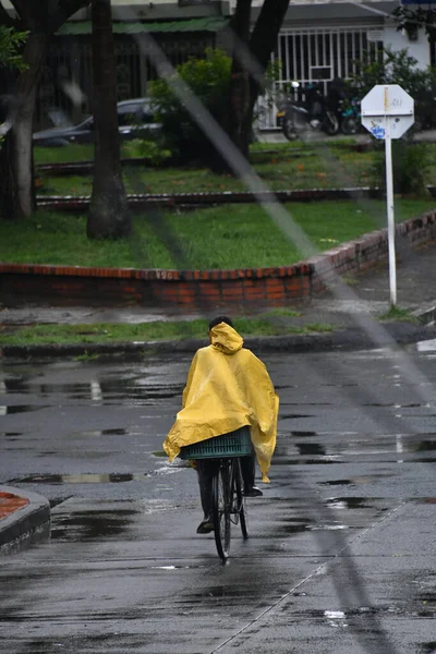 Sarı pelerinli bisikletli bir adam kendini yağmurdan koruyor.