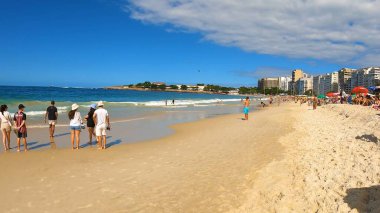 Kalabalık, dünyaca ünlü bir sahil bölgesindeki parlak güneşli gökyüzü altında yürüyüş, yüzme, rahatlık ve seyahat havasının tadını çıkarıyor. 13 Nisan 2024, Copacabana Plajı, Rio de Janeiro, Brezilya.
