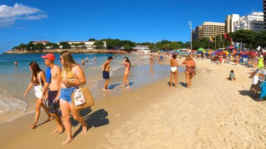 Kalabalık, dünyaca ünlü bir sahil bölgesindeki parlak güneşli gökyüzü altında yürüyüş, yüzme, rahatlık ve seyahat havasının tadını çıkarıyor. 13 Nisan 2024, Copacabana Plajı, Rio de Janeiro, Brezilya.