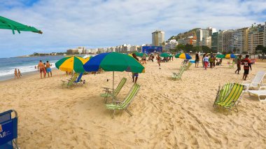 Kalabalık, dünyaca ünlü bir sahil bölgesindeki parlak güneşli gökyüzü altında yürüyüş, yüzme, rahatlık ve seyahat havasının tadını çıkarıyor. 13 Nisan 2024, Copacabana Plajı, Rio de Janeiro, Brezilya.