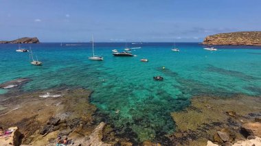 Kumsala gidenler güneşli havanın, berrak suların ve popüler bir adada tatil ve seyahat havasının tadını çıkarıyorlar. 13 Nisan 2023, İbiza Adası, İspanya.