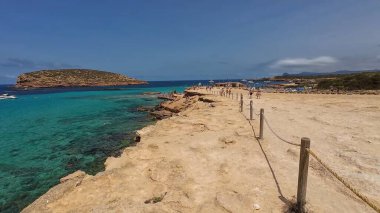 Kumsala gidenler güneşli havanın, berrak suların ve popüler bir adada tatil ve seyahat havasının tadını çıkarıyorlar. 13 Nisan 2023, İbiza Adası, İspanya.