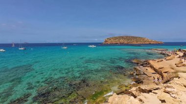 Kumsala gidenler güneşli havanın, berrak suların ve popüler bir adada tatil ve seyahat havasının tadını çıkarıyorlar. 13 Nisan 2023, İbiza Adası, İspanya.