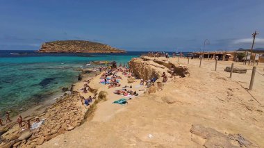 Kumsala gidenler güneşli havanın, berrak suların ve popüler bir adada tatil ve seyahat havasının tadını çıkarıyorlar. 13 Nisan 2023, İbiza Adası, İspanya.