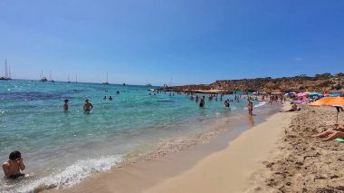 Kumsala gidenler güneşli havanın, berrak suların ve popüler bir adada tatil ve seyahat havasının tadını çıkarıyorlar. 13 Nisan 2023, İbiza Adası, İspanya.