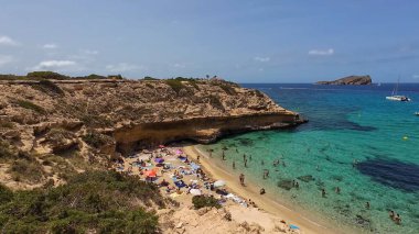 Kumsala gidenler güneşli havanın, berrak suların ve popüler bir adada tatil ve seyahat havasının tadını çıkarıyorlar. 13 Nisan 2023, İbiza Adası, İspanya.