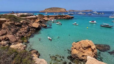 Kumsala gidenler güneşli havanın, berrak suların ve popüler bir adada tatil ve seyahat havasının tadını çıkarıyorlar. 13 Nisan 2023, İbiza Adası, İspanya.