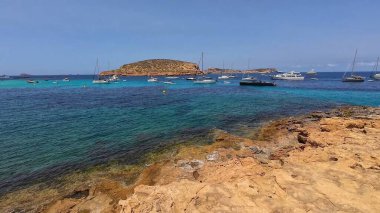 Kumsala gidenler güneşli havanın, berrak suların ve popüler bir adada tatil ve seyahat havasının tadını çıkarıyorlar. 13 Nisan 2023, İbiza Adası, İspanya.