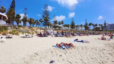 İnsanlar tatil tatili, tur, seyahat, yüzme, oyun, yürüyüş, yemek ve güneşli gökyüzü ve mavi-beyaz bulutlar altında dinlenme ile yaşam tarzları ve plaj titreşimleri. Ayia Napa Adası, Kıbrıs - 8 Temmuz 2023.
