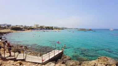 Canlı sahil titreşimleri, berrak mavi sular, kumlu kıyılar, güneşli gökyüzü, ve manzaralı güzellik, tatil için ideal eğlence, tur, seyahat ve rahatlama. İncir Ağacı Sahili, Protaras, Kıbrıs - 13 Temmuz 2023.