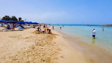 Canlı sahil titreşimleri, berrak mavi sular, kumlu kıyılar, güneşli gökyüzü, ve manzaralı güzellik, tatil için ideal eğlence, tur, seyahat ve rahatlama. İncir Ağacı Sahili, Protaras, Kıbrıs - 13 Temmuz 2023.