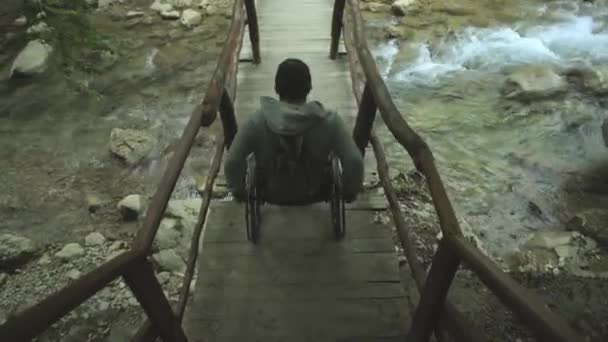 Muž na invalidním vozíku na lávce v horách — Stock video