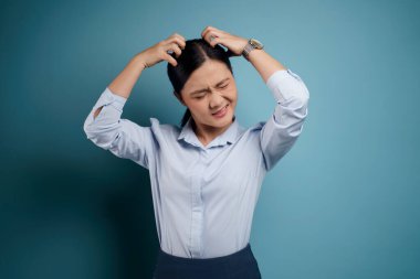 Asyalı kadın sıkılmış ve canı sıkkın, kafasını kaşıyor, mavi arka planda soyutlanmış..